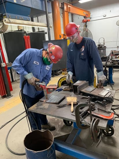 An instructor watches a student perform a welding operation in the High Steel University workshop.